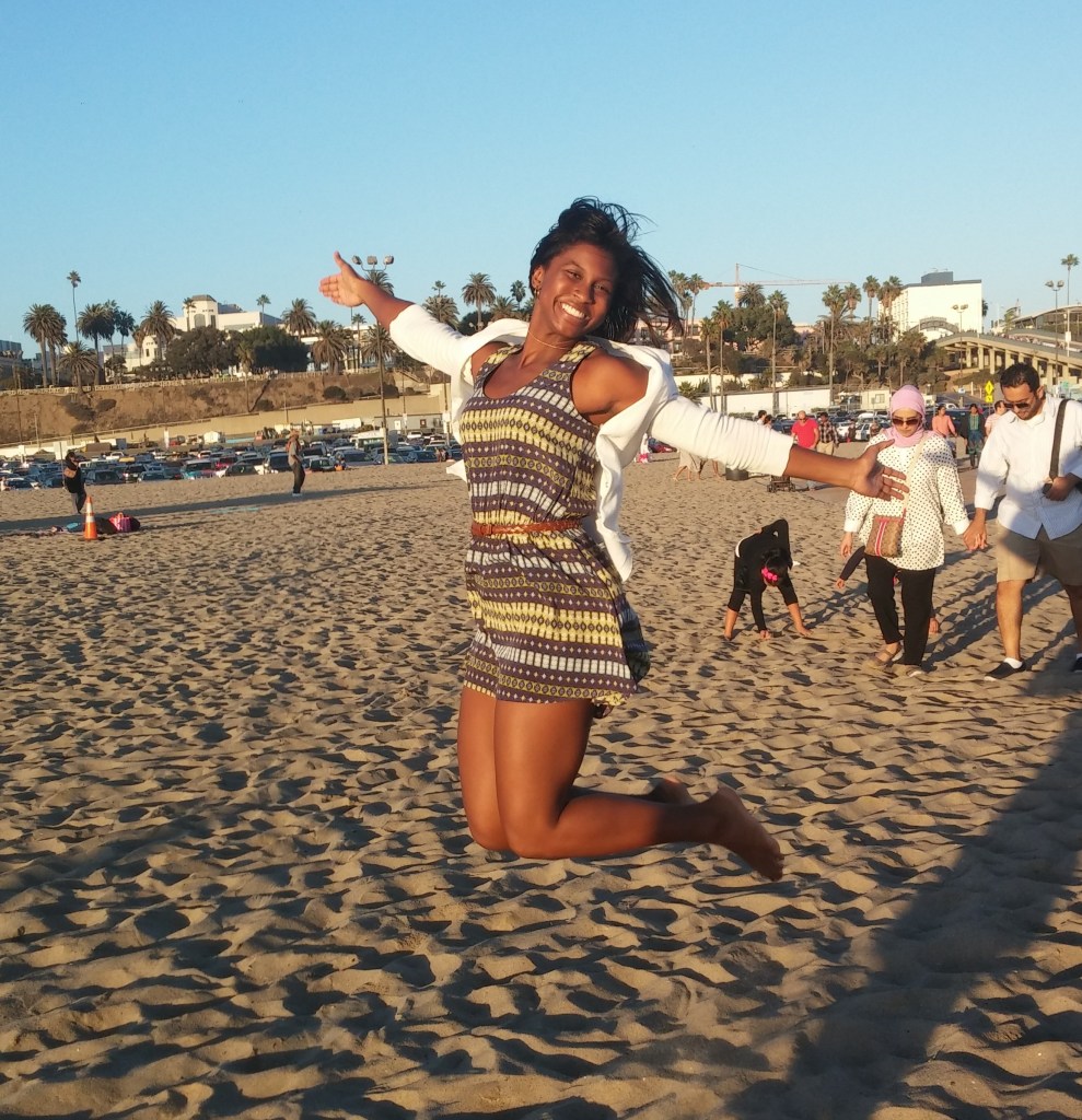 girl jumping and smiling in the sunshine and sand at the beach